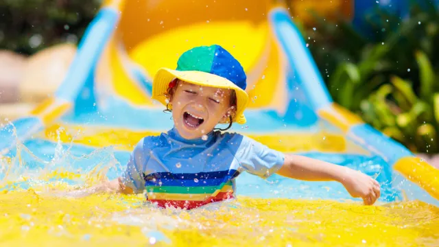 Child gleefully sliding down a colorful water slide in a swimming pool.