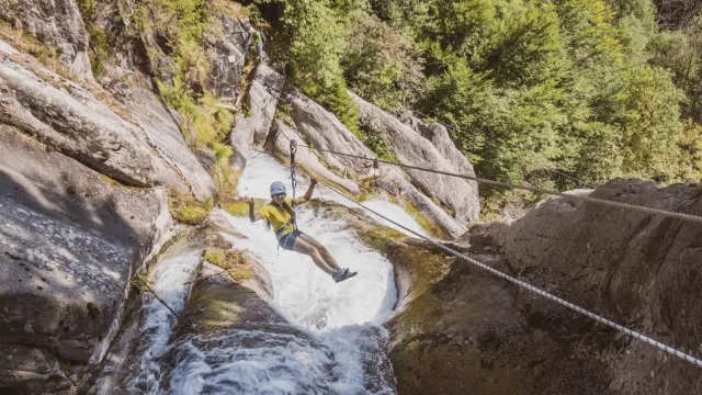 Person rappelling down a rocky waterfall in a lush forest.
