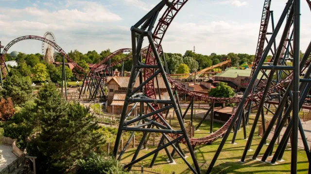 Roller coaster with loops in a theme park setting, under a partly cloudy sky.