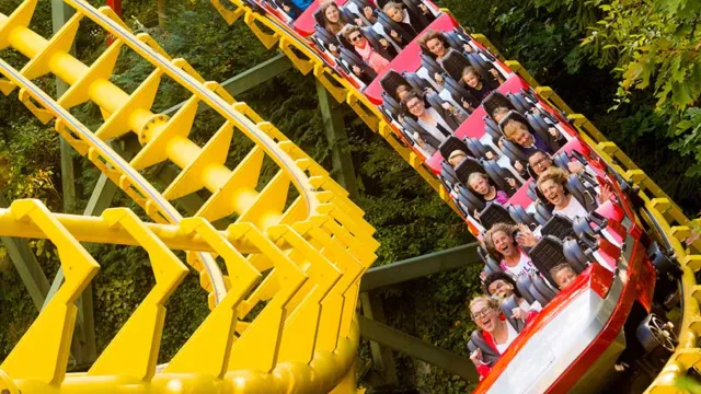 Roller coaster with yellow tracks and riders in a red car, surrounded by green foliage.