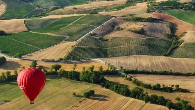 Red hot air balloon above patchwork fields and rolling hills.