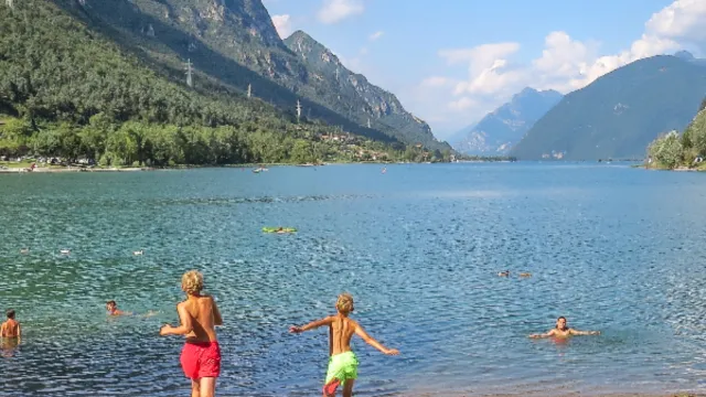 Children playing by a mountain lake under a clear blue sky.