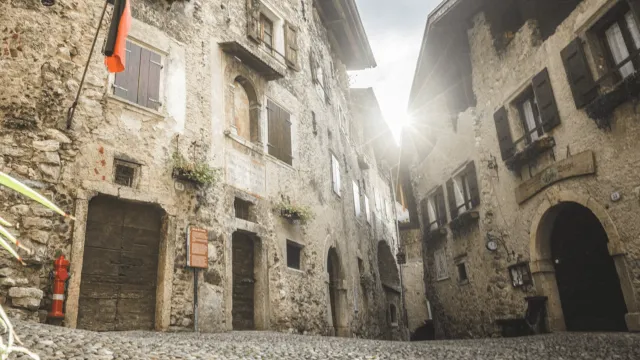 Stone buildings in a narrow alleyway, sunlight shining between them.