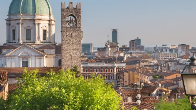Cityscape with domed cathedral and clock tower, lush greenery in foreground.
