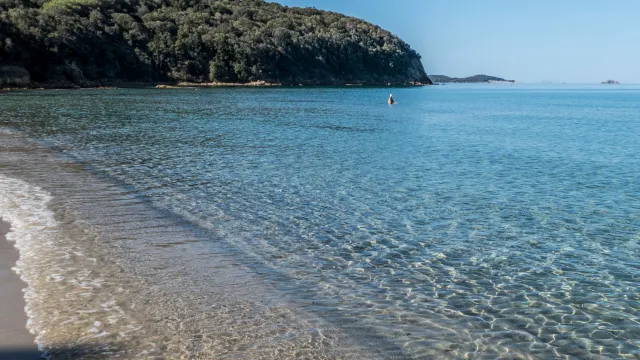 Calm beach with clear water, distant hills, and a blue sky.