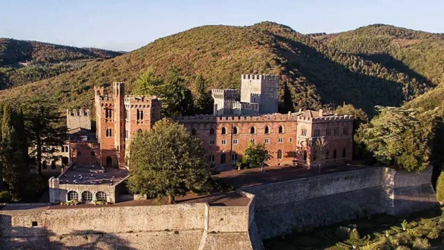 Castle in a hilly landscape with lush greenery under a clear blue sky.