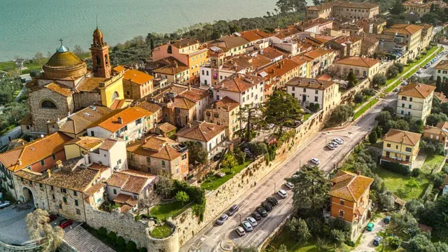 Historic coastal town with terracotta rooftops, surrounded by lush greenery and sea.