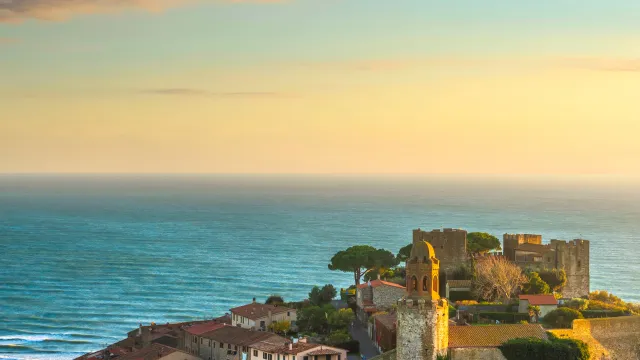 Coastal medieval town at sunset, with sea and castle ruins.