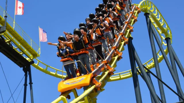 Roller coaster with riders on a steep track under a clear blue sky.