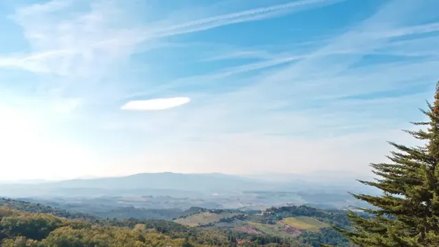 Cyclist on a rural road with a vast, scenic landscape under a clear blue sky.