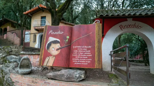 Pinocchio mural in a wooded park setting near a small house and archway.