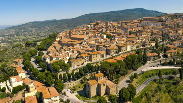 Aerial view of a hilly town with terracotta roofs and lush greenery.