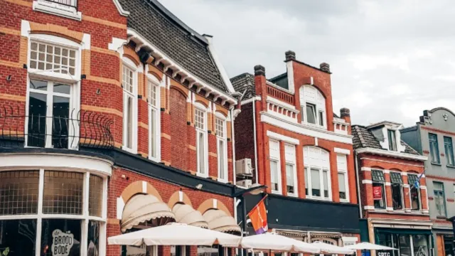 Historic street with red brick buildings, outdoor cafes, and people walking.