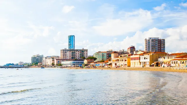 Sunny beachfront with city skyline, clear sky, and gentle waves.