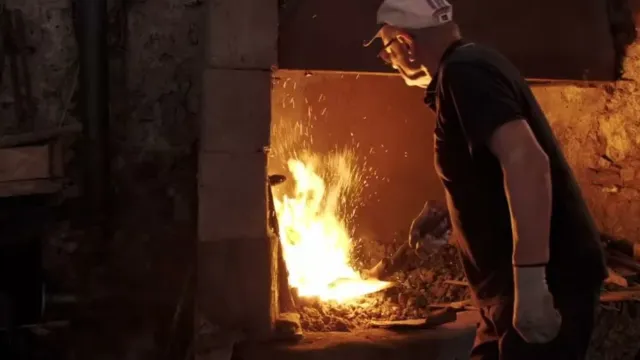 Blacksmith working by a forge with bright flames.