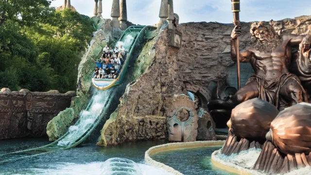 Water ride with riders descending a sculpted slide, large Neptune statue nearby.