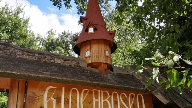 Wooden entrance with a small pointed tower, surrounded by lush greenery.