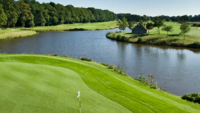 Golf course with green, river, and trees under clear blue sky.
