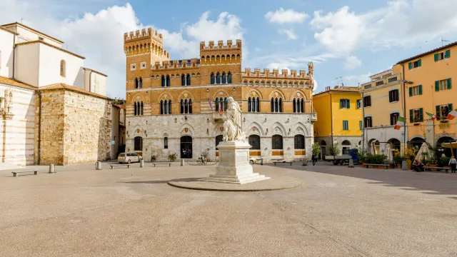 Sunny European square with historic buildings and central statue.