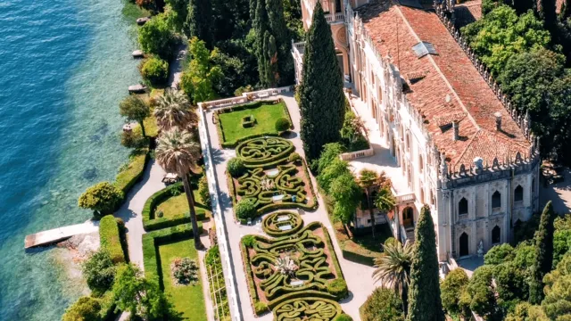 Aerial view of a lakeside villa with intricate gardens and lush greenery.