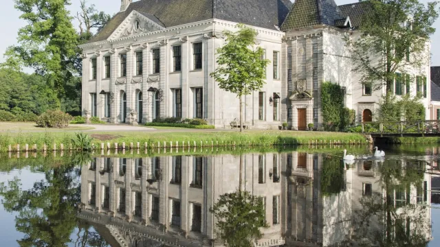 Elegant manor house reflected in a calm lake, surrounded by trees.