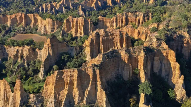 Rocky landscape with tall, jagged cliffs, green vegetation, and distant hills.