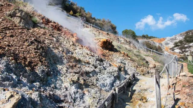 Steaming hillside with wooden walkways under a clear blue sky.
