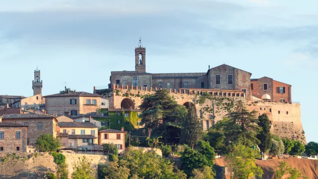 Hilltop town with stone buildings and lush trees under a clear blue sky.