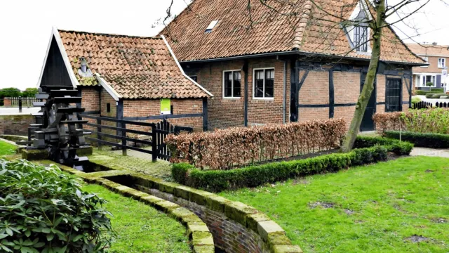 Historic brick house with a red-tiled roof, black beams, and a small water channel.