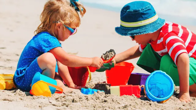 Kids in summer clothes playing in sand on a sunny beach.