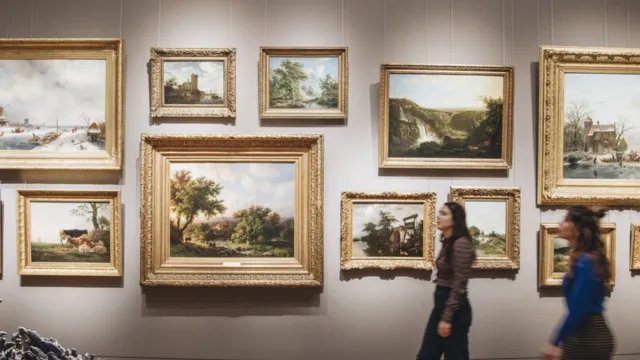 Art gallery with framed paintings and two people walking.