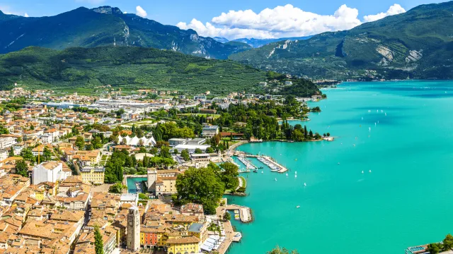 Aerial view of a town by a turquoise lake, surrounded by mountains under a blue sky.