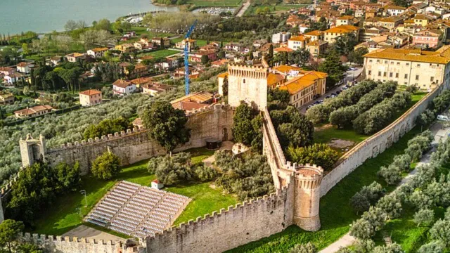 Medieval castle with walls, surrounded by lush greenery and a town in the background.