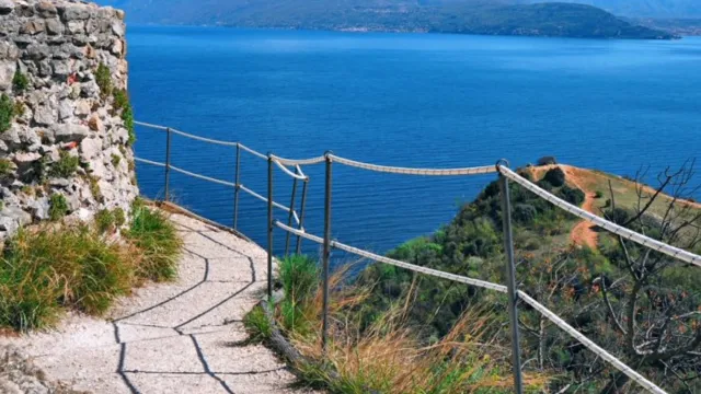 Hilltop path overlooking blue sea and distant mountains under a clear sky.
