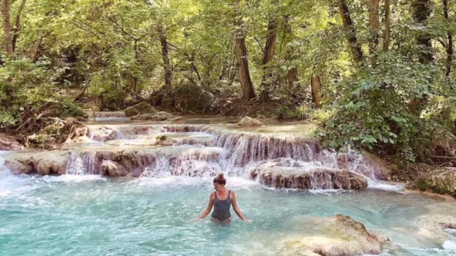 Person standing in a serene forest waterfall pool.
