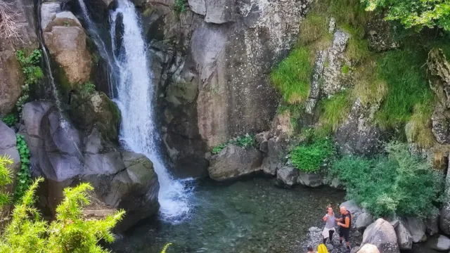 Waterfall cascading into a rocky pool with people gathered nearby.