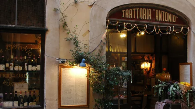 Cozy Italian trattoria entrance with outdoor table, wine display, and plants.