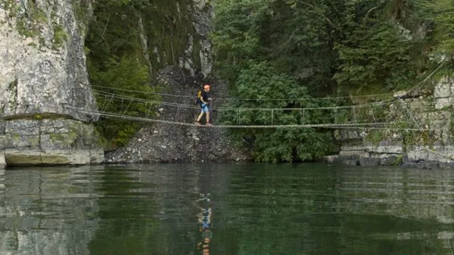 Suspension bridge over a green river between rocky cliffs.