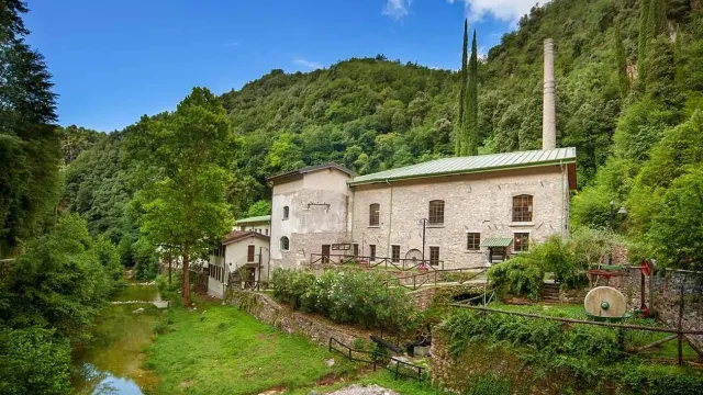 Historic stone building surrounded by lush green hills under a bright blue sky.