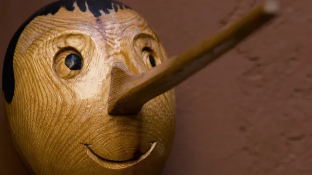 Wooden Pinocchio sculpture with a long nose against a brown wall.