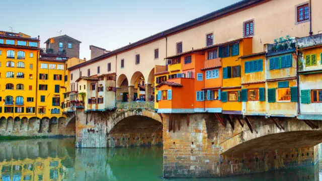Colorful historic bridge over calm river under blue sky.