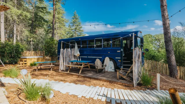 Blue bus converted into a cozy outdoor seating area in a forest setting.