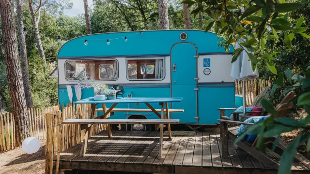 Teal caravan on a wooden deck surrounded by trees.