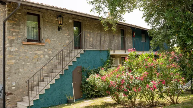 Stone building with stairs, surrounded by greenery and flowering bushes.