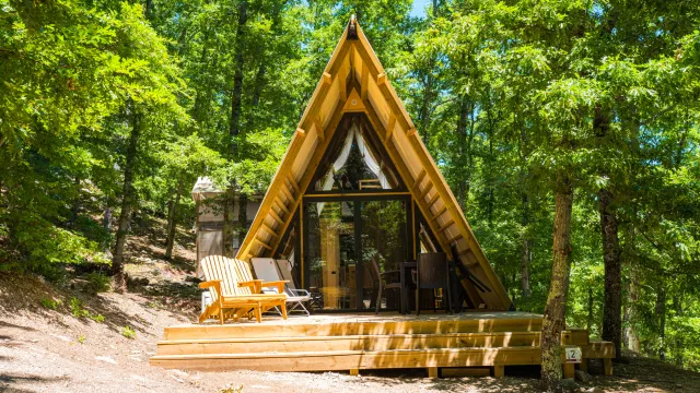 A-frame cabin in a forest, with a small deck and chairs.