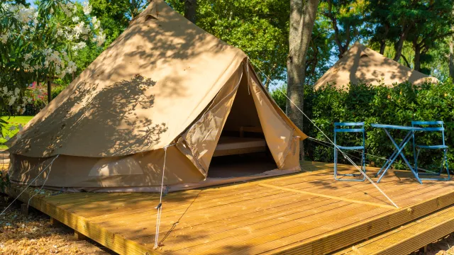 Tent on wooden platform surrounded by trees, with two blue folding chairs.