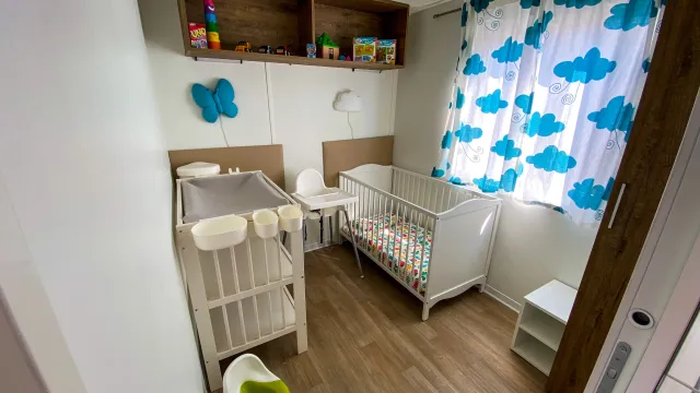 Compact nursery with crib, changing table, cloud-pattern curtains, and toys on shelves.