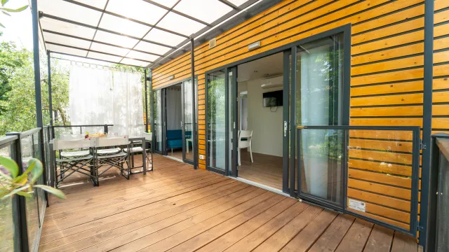 Wooden patio with table, chairs, and sliding doors under a clear roof.