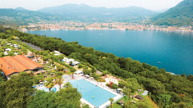 Aerial view of a pool beside a lake, surrounded by trees and mountains in the distance.
