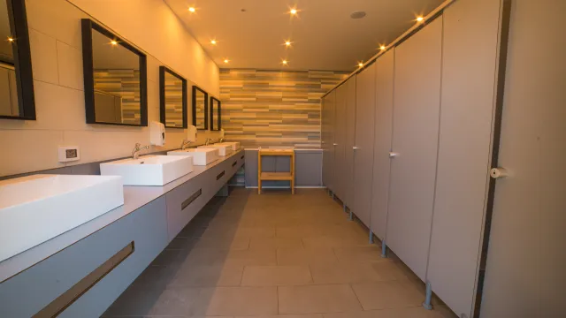 Modern restroom with sinks, mirrors, and stalls. Warm lighting and tiled walls.